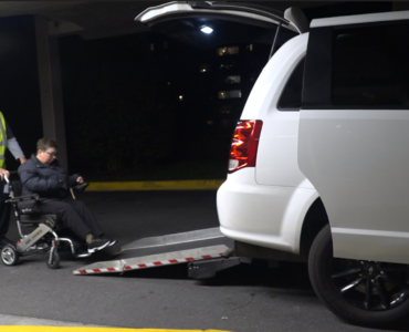Wheelchair user Kelly Mack being helped into a wheelchair accessible Uber via a back door ramp